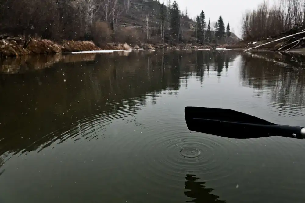 Close up of a wooden paddle dipping into calm lake water